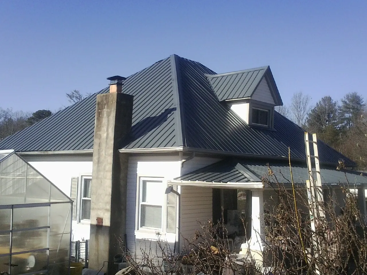 Dark blue standing seam metal roof on a white farmhouse with dormer — Slate & Tile Roof Repair by Roofing Brothers in Keysville