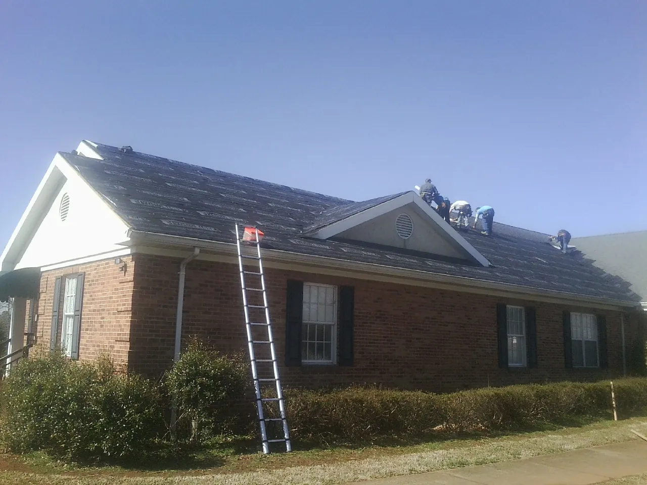 Crew tearing shingles off a brick ranch roof with a ladder set — Metal Roof Repair work by our crew in Keysville