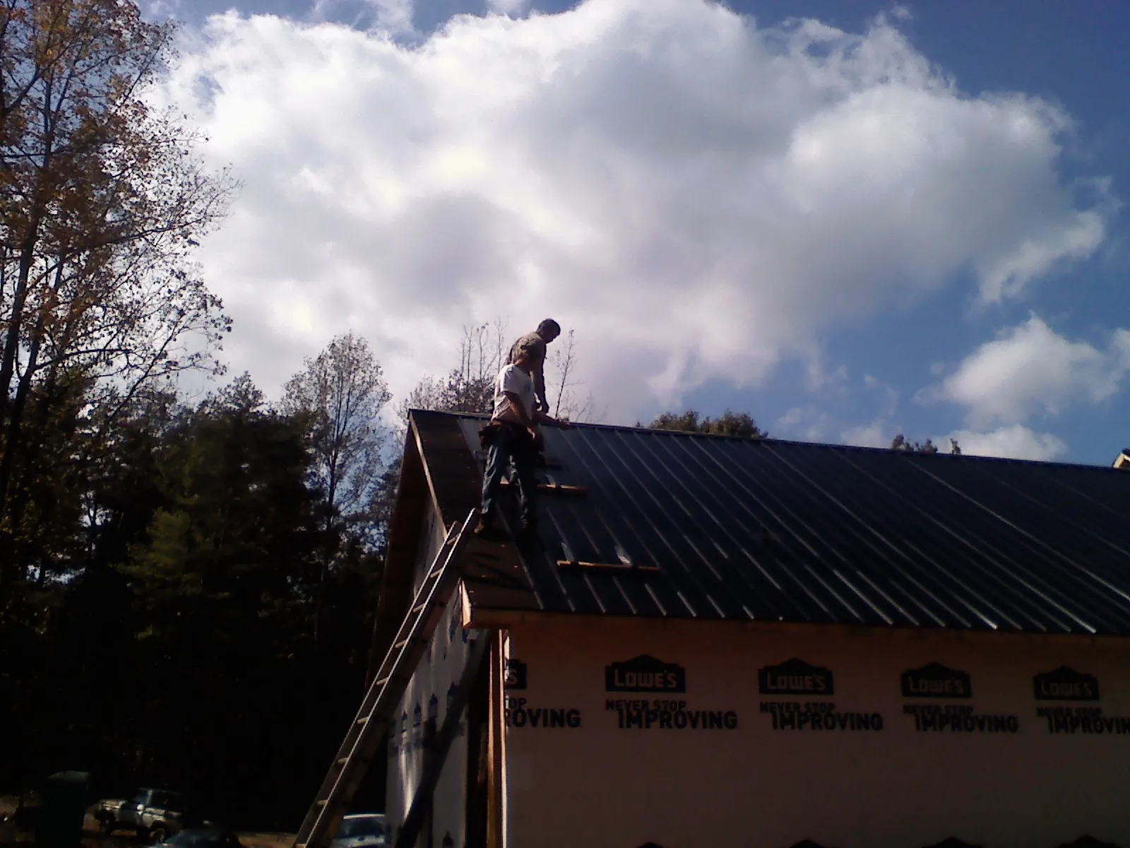 Roofer fastening dark metal panels high against a cloudy sky, from a Roof Inspection job in Keysville